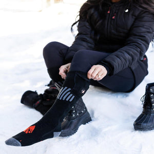 Person wearing black ActionHeat battery heated socks while sitting in the snow