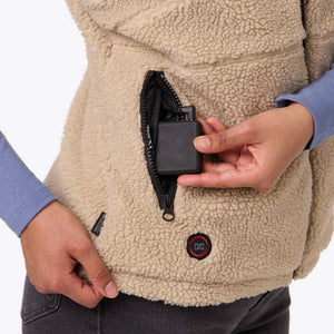 Hand placing a Mobile Warming battery pack into the zippered pocket of a tan fleece vest