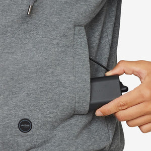 Hand placing a black Venture Heat battery pack into the pocket of a grey hooded sweatshirt