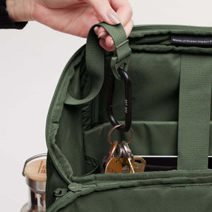 Hand holding a key ring attached to a black carabiner inside a green backpack