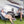 Portable desk fan on a folding table between two people sitting in camping chairs outside a recreational vehicle
