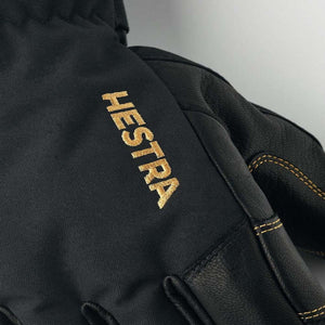 Black Hestra glove with gold embroidered logo and stitching