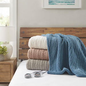 Stack of three textured heated blankets in white tan and grey with blue blanket draped over and two remote controllers