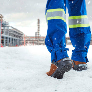 Worker wearing blue high visibility trousers and ice cleats on boots walking in snow