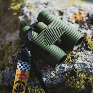 Olive green binoculars with a patterned strap resting on a mossy rock