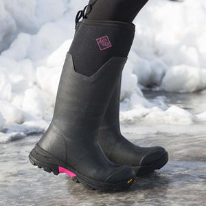 Black Muck tall rubber boots with pink logo and sole detail standing in snow