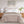 Beige quilted throw blanket draped over a bed with white pillows and wooden nightstands