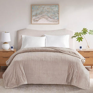 Beige quilted throw blanket draped over a bed with white pillows and wooden nightstands