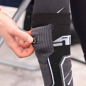 Hand pressing the power button on a black heated compression calf sleeve