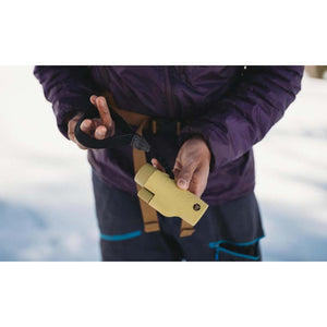 Person holding a tan monocular with a wrist strap in a snowy environment