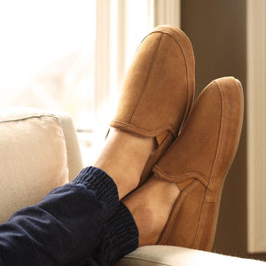 Acorn tan suede slip on slippers worn on feet resting on a couch