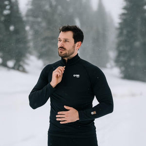 Man wearing a black Gobi Heat long sleeve quarter zip base layer in a snowy forest