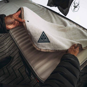 Hands holding an Ignik branded fleece blanket over a sleeping pad