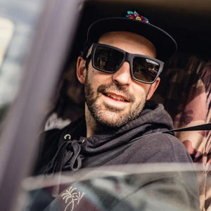 Man wearing black sunglasses and a baseball cap sitting in a vehicle