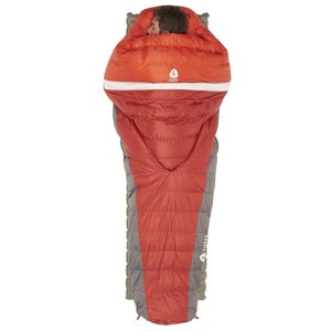 Person sleeping in a red and grey Sierra Designs mummy sleeping bag on a green sleeping pad
