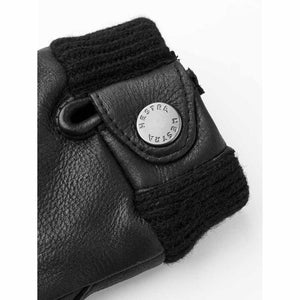 Close up of black Hestra leather glove cuff with ribbed knit trim and branded metal snap button