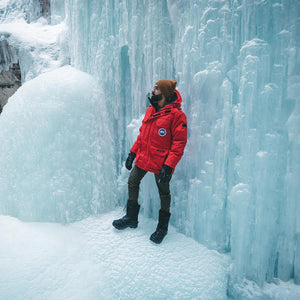 Person wearing a red Canada Goose parka and brown beanie standing in front of a frozen waterfall