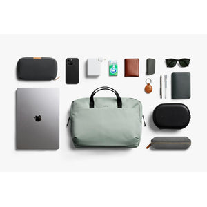 Bellroy bag surrounded by laptop phone charger gum wallet keys pens sunglasses and cases on white background