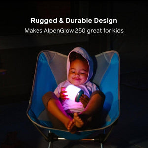Child sitting in a blue camping chair holding a glowing BioLite AlpenGlow 250 lantern at night