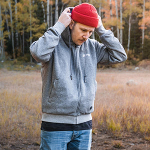 Man wearing a grey zip up hoodie and a red beanie in a forest setting