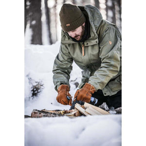 Person wearing Hestra leather gloves while preparing firewood in a snowy forest