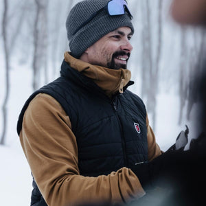 Man wearing a FjallRaven black vest and brown sweater in a snowy forest