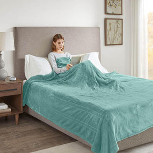 Person reading a book in bed covered by a teal plush blanket