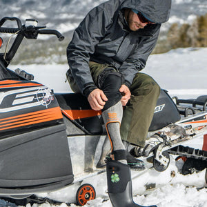 Person sitting on a snowmobile pulling on a Mobile Warming heated sock