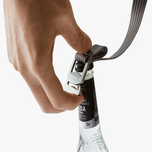 Hand using a Bellroy bottle opener attached to a strap to open a glass soda bottle