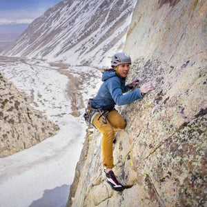 Climber wearing Black Diamond helmet and gear ascending a steep rock face above a snowy valley