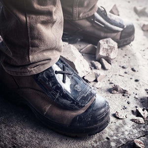 Work boots with black Metguard protective covers on concrete with debris