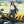 Woman wearing California Heat leather pants and white shirt standing by a yellow three-wheeled motorcycle