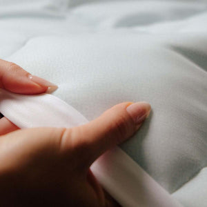 Close up of hands holding the edge of an Outlast white fabric bedding item