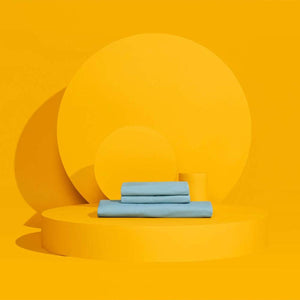 Outlast light blue folded bed sheets on a yellow circular platform