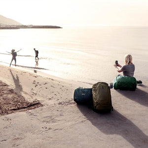 Thule backpacks and duffel bags on a beach with people in the background