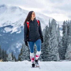 Woman wearing black puffer jacket blue leggings and patterned knee high socks standing in snowy mountain landscape
