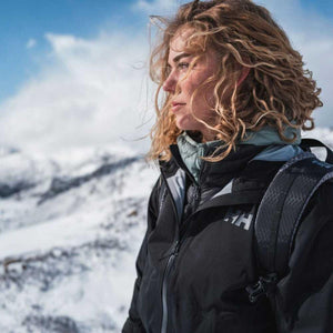 Woman wearing a Helly Hansen black jacket and backpack in a snowy mountain landscape