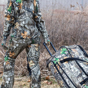 Person wearing DSG Outerwear camouflage hunting gear pulling a matching rolling duffel bag