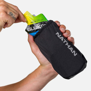 Hand holding a Glukos lemon lime energy liquid gel packet inside a black Nathan branded sleeve