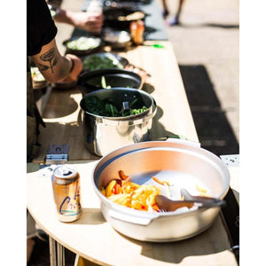 Person cooking vegetables in metal pots on a wooden outdoor table