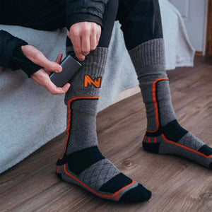 Person inserting a Mobile Warming battery pack into the pocket of a grey and orange heated sock