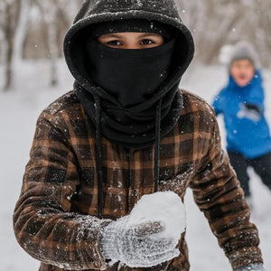 Child wearing Gobi Heat plaid shirt and black face mask holding a snowball in snowy weather