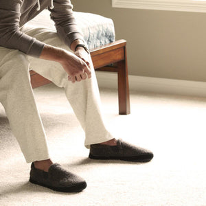 Person wearing Acorn dark grey wool slippers while sitting on a wooden bench