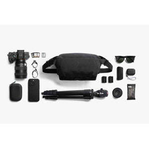 Bellroy black sling bag surrounded by camera gear including a Sony camera lens tripod and accessories