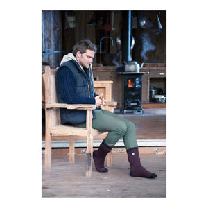 Man wearing Heat Holders socks sitting on a wooden chair in a rustic cabin