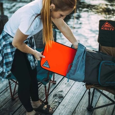 Person placing an Ignik orange fire pit into a Kelty camping chair bag on a wooden dock