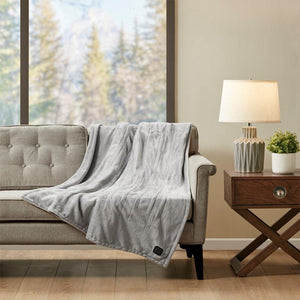 Grey heated throw blanket draped over a sofa next to a side table with a lamp