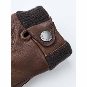Close up of brown Hestra leather glove cuff with ribbed knit trim and branded metal snap button