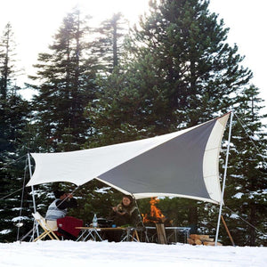 Snow Peak tarp set up over a table and chairs in a snowy forest with a campfire