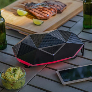 Outdoor Tech geometric black portable speaker with red LED base on a table with food